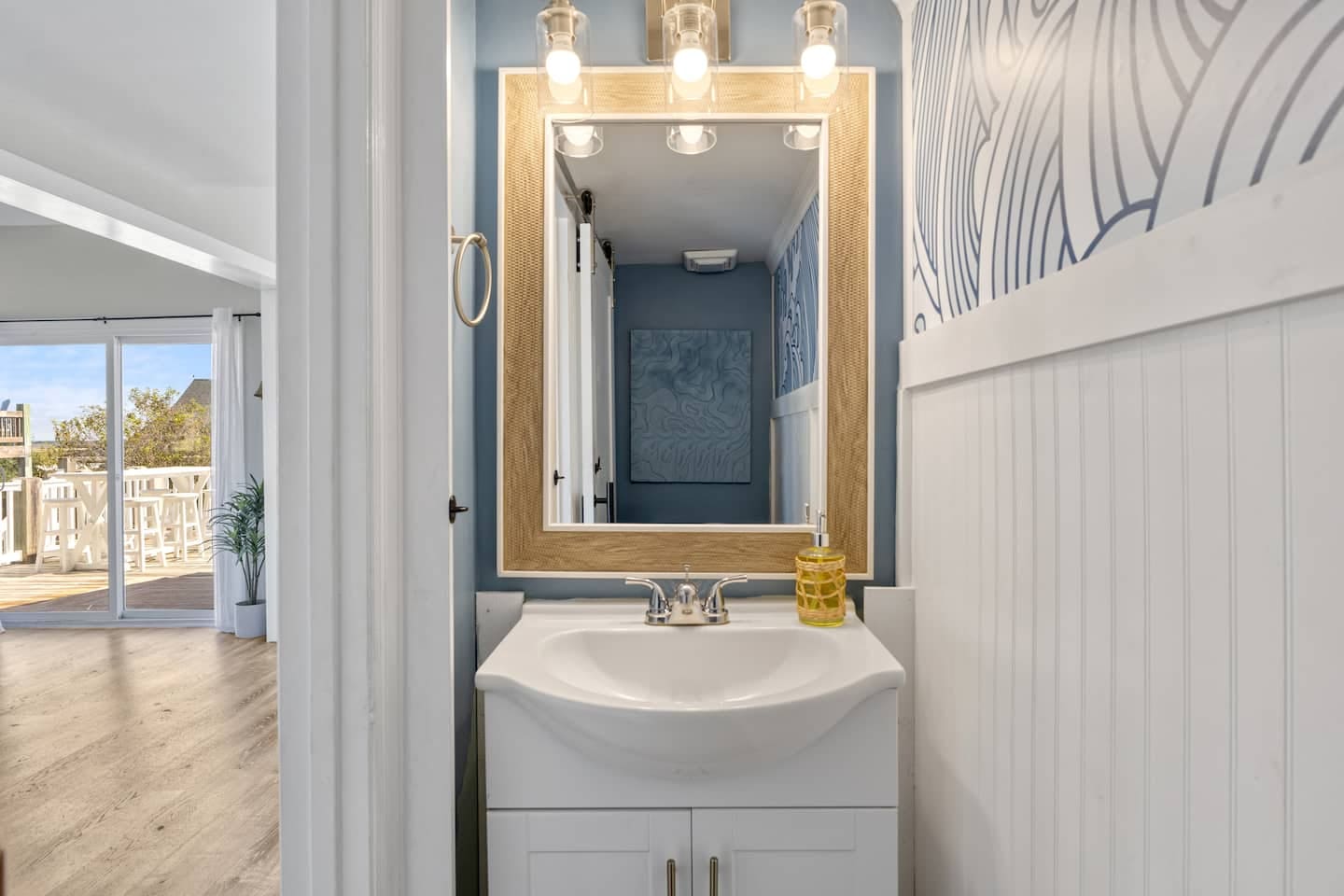 Powder room with coastal blue walls and woven mirror